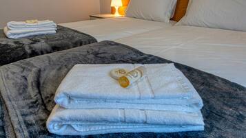 A neatly made bed with white linens and a rolled towel on a dark, textured ottoman.