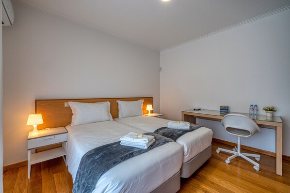 A hotel room with two beds, a desk, a chair, and a nightstand with lamps. - Central Suites Arouca (Arouca)