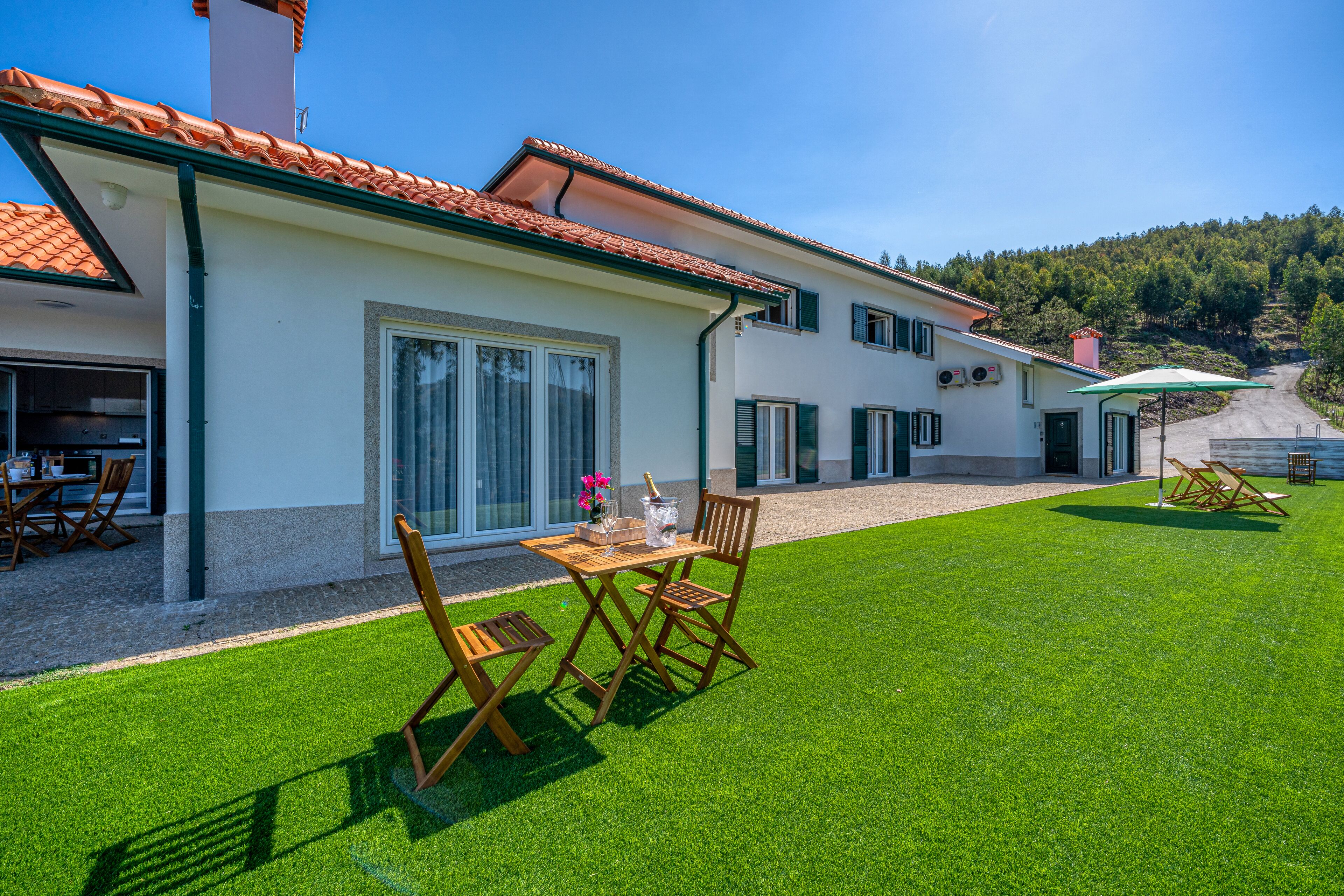 A two-story house with a tiled roof, a well-maintained lawn, and a dining area with outdoor furniture.