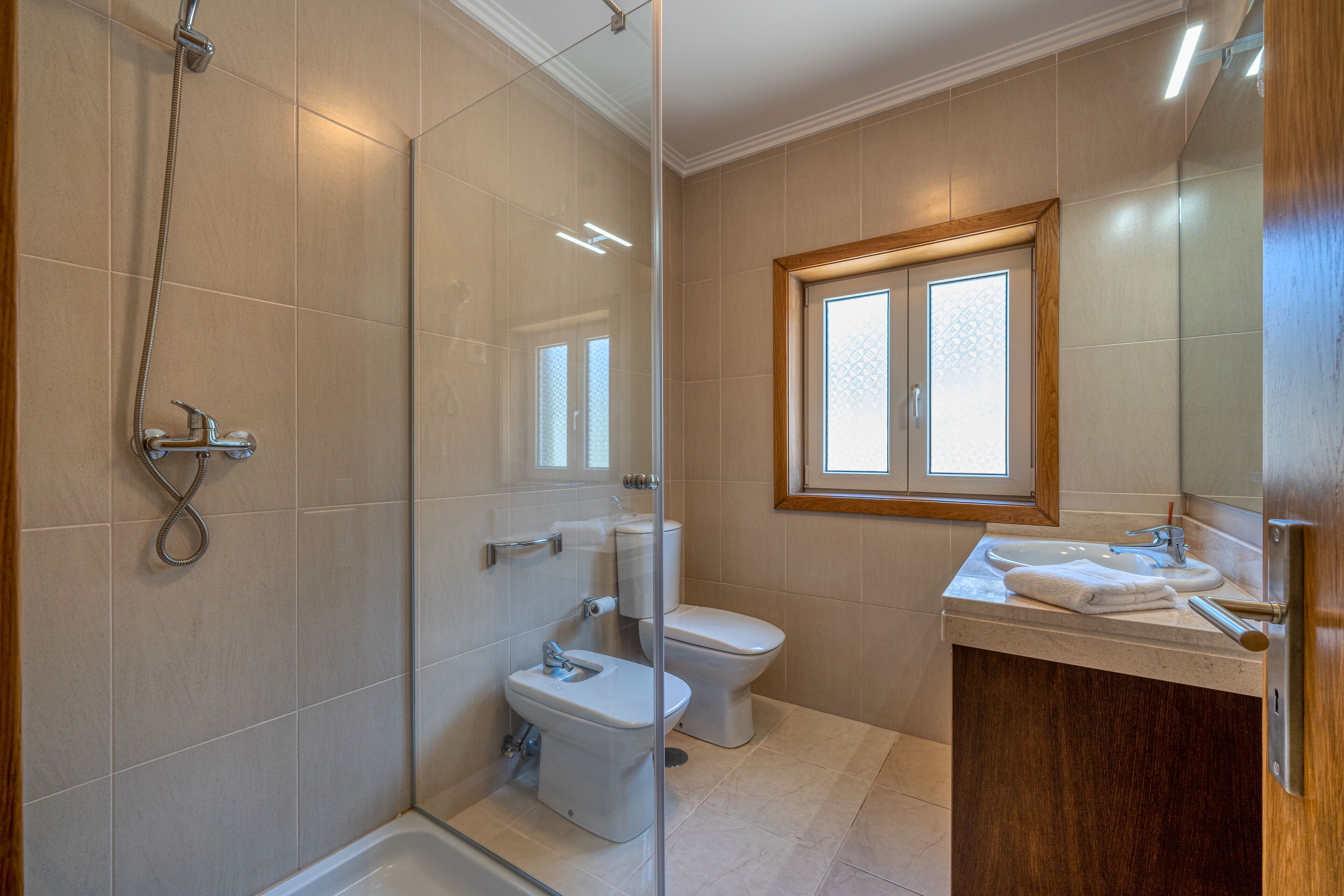Une salle de bain moderne dotée d’une douche à parois de verre, de toilettes et d’un lavabo avec un meuble-vasque en bois.