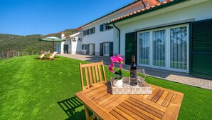 A well-maintained lawn with two wooden chairs and a table set for dining, a bottle of wine, and a vase with flowers. - Central Suites Arouca (Arouca)