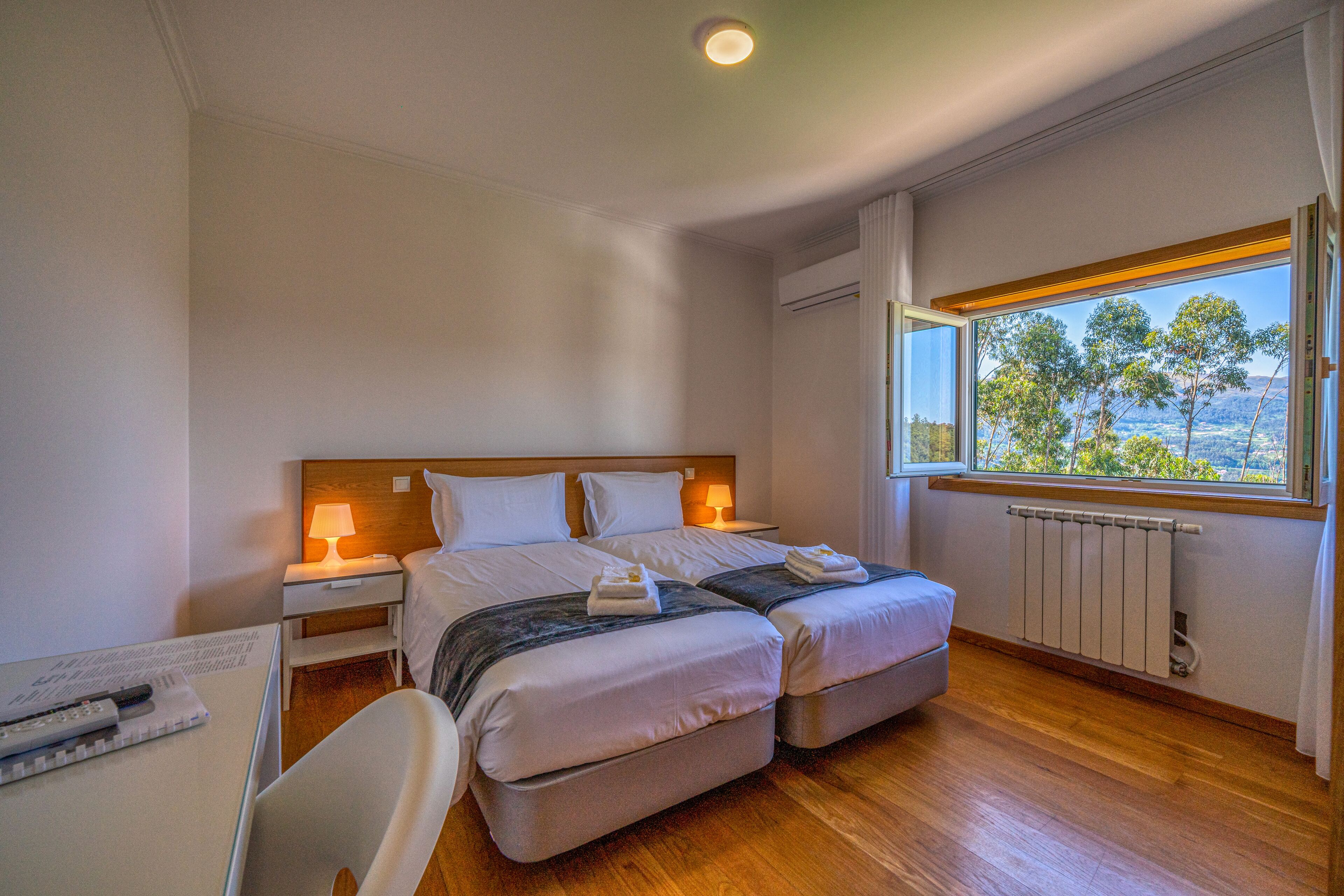 Une chambre d’hôtel avec deux lits, un bureau et une fenêtre donnant sur des arbres et des collines.