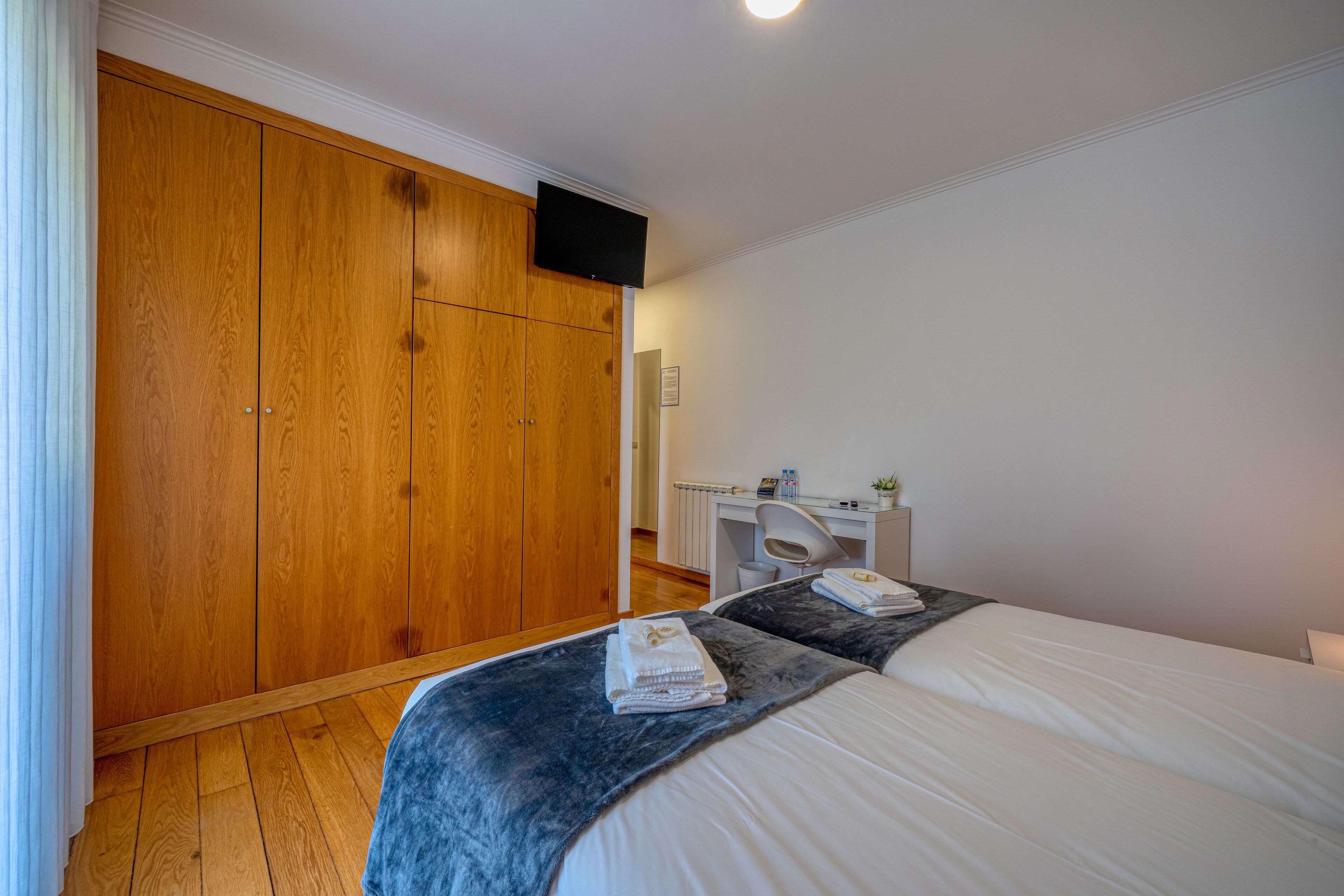 Un dormitorio con un armario grande de madera, un escritorio con una silla y una cama con una colcha azul.
