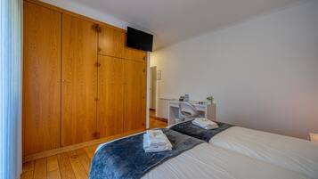 Un dormitorio con un armario grande de madera, un escritorio con una silla y una cama con una colcha azul.