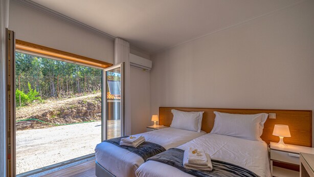 A hotel room with two beds, a large window with a view of a forested area, and a wooden headboard. - Central Suites Arouca (Arouca)