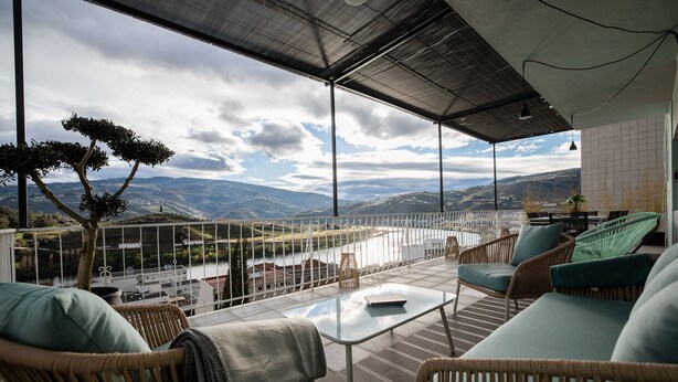 Een balkon met rieten meubilair, een glazen tafel en uitzicht op het landschap.