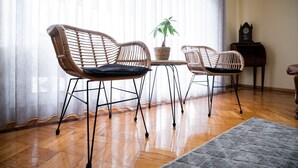 Een kamer met rieten stoelen, een tafeltje, een plant in pot en een houten kast.