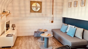 Un dormitorio estilo loft acogedor con techo inclinado, decoración de pared de madera, un remo de madera colgante, una mesa redonda con una cesta tejida, un sofá gris con cojines azules y blancos, y una lámpara colgante.