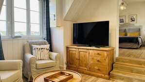 Una sala de estar acogedora con televisor, sofá, sillón, aparador de madera y una mesita de mimbre.
