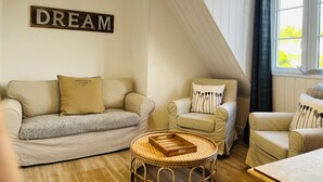 Una habitación acogedora con techo estilo loft, un sofá, una silla y una pequeña mesa redonda. Un letrero en la pared dice "DREAM".