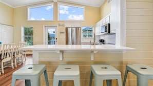 A kitchen with a large island, white cabinets, stainless steel appliances, and a view of a building through a window.