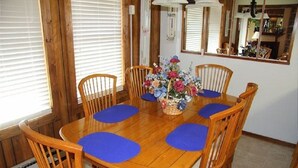 Une table à manger en bois, agrémentée de sets de table bleus, est entourée de chaises en bois. Un vase rempli de fleurs est posé sur la table.