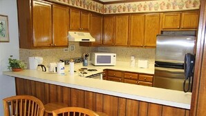 Une cuisine avec des meubles de rangement en bois, un réfrigérateur en acier inoxydable, un four à micro-ondes et une machine à café. On y trouve deux chaises en bois et une petite table sur laquelle est posé un vase de fleurs.