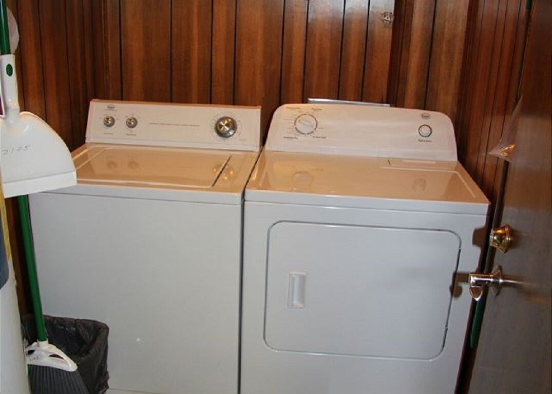 A front-loading washer and dryer unit with a wooden panel wall behind it.