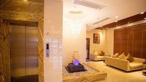 A lobby with a marble wall, an elevator, a chandelier, a sofa set, and a decorative vase. - Jiayu Business Hostel (Sihui)