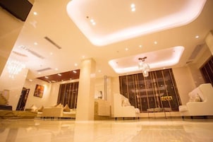 A modern hotel lobby with a high ceiling, recessed lighting, and a central chandelier.