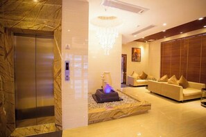 A lobby with a marble wall, an elevator, a seating area with a sofa and cushions, and a decorative fountain. - Jiayu Business Hostel (Sihui)