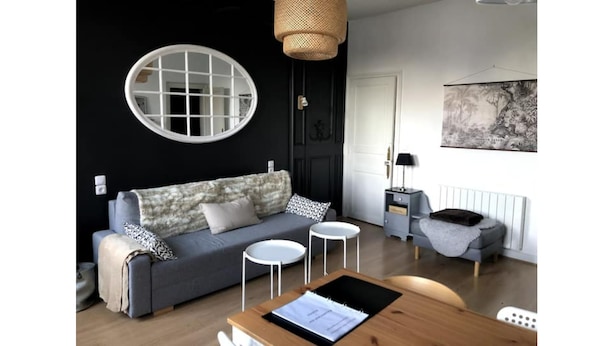 Una sala de estar moderna con un sofá gris, un espejo redondo, una mesita redonda y una mesita auxiliar con una lámpara.