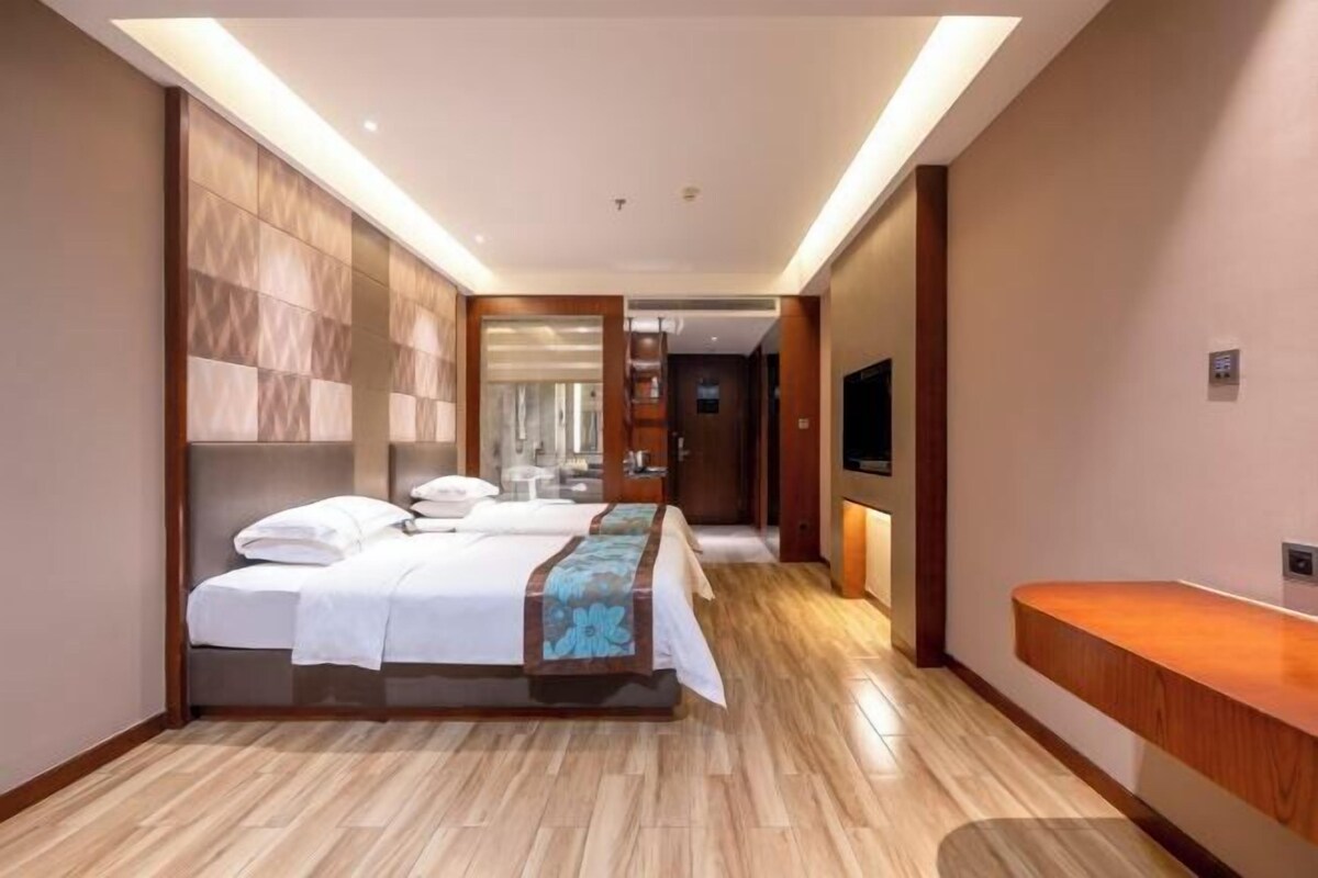 A modern hotel room with a large bed, a wooden headboard, a bedside table, and a TV mounted on the wall.