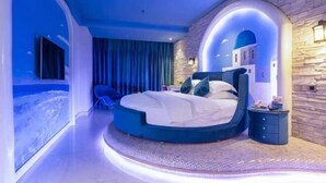 Un dormitorio moderno con una cama curvada, una pared de acento de piedra y vistas al mar.