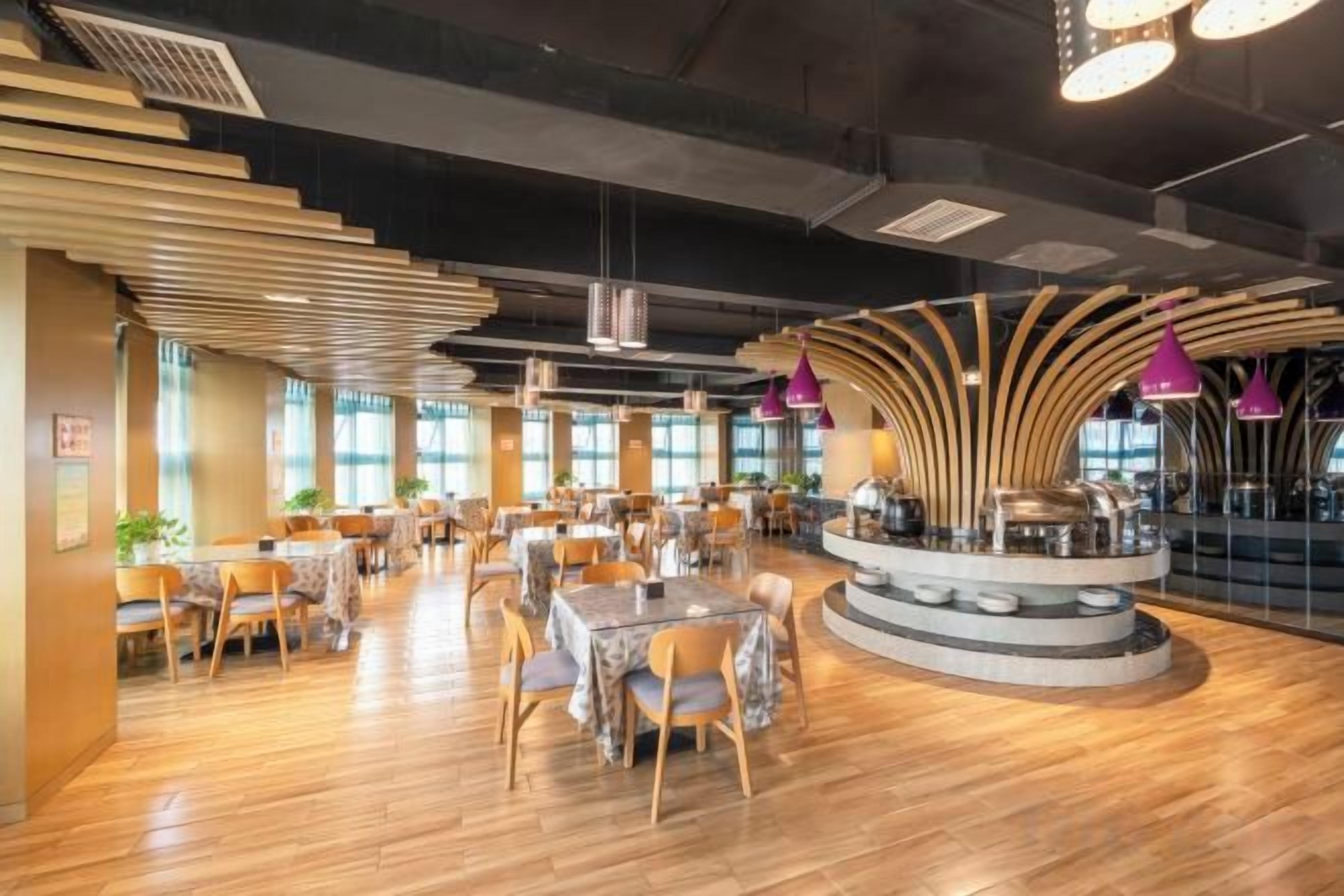 Un restaurante amplio con numerosas mesas y sillas, una barra central y grandes ventanales que dejan entrar luz natural.