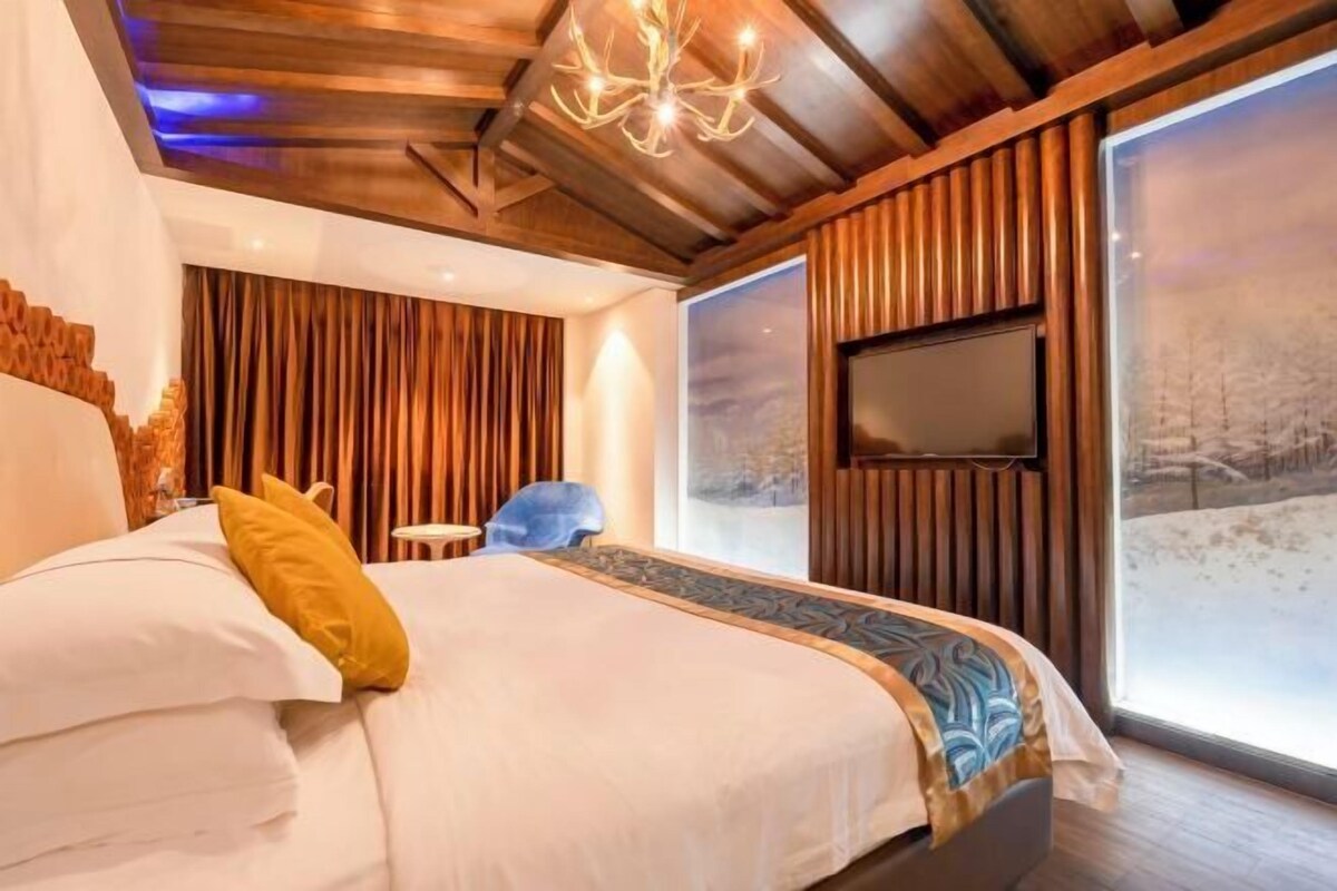 A bedroom with a bed, a TV mounted on the wall, and a large window with a view.