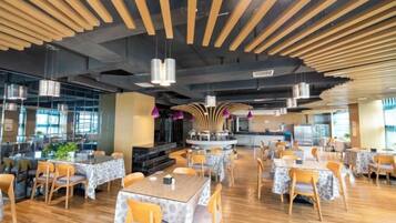 A spacious restaurant with wooden flooring, multiple tables and chairs, and pendant lighting.