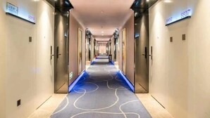 Pasillo de hotel con alfombra estampada, puertas metálicas y letreros iluminados que indican los números de las habitaciones.