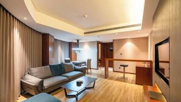 A modern hotel room with a sofa, coffee table, and a desk area.