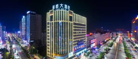 Un hôtel à plusieurs étages, doté d’une enseigne lumineuse, situé dans une rue animée de la ville et éclairé la nuit.