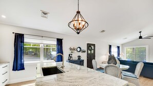 A modern kitchen with a marble countertop, a chandelier, and a dining area with wicker chairs. - Greenbriar Getaway: Quaint Cottage in Canandaigua (Canandaigua)
