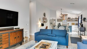 A modern living room with a large flat-screen TV, a blue sofa, and a coffee table with remote controls. - Greenbriar Getaway: Quaint Cottage in Canandaigua (Canandaigua)