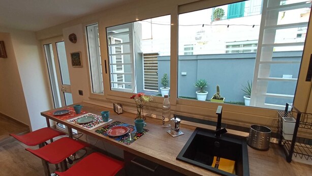 A modern kitchen with a large island, red bar stools, and large windows offering a view of the city. - Cappucci Garden House, nice apartment with little garden few steps from seafront (Pozzuoli)