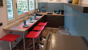 A compact kitchen with a long counter, red bar stools, a coffee machine, and a stone wall. - Cappucci Garden House, nice apartment with little garden few steps from seafront (Pozzuoli)