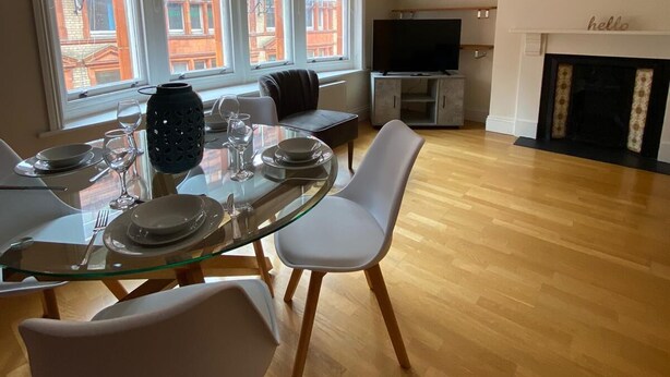 A dining area with a glass table, white chairs, and a TV in the background. - Monthly, Short, Stays 2-bed Apartment in Reading (Reading)