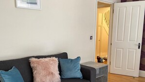 A grey sofa with three cushions, a wooden floor, a white door, and a patterned wall. - Monthly, Short, Stays 2-bed Apartment in Reading (Reading)