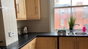 A kitchen with wooden cabinets, a black countertop, a stainless steel sink, and a window with a view of buildings. - Monthly, Short, Stays 2-bed Apartment in Reading (Reading)