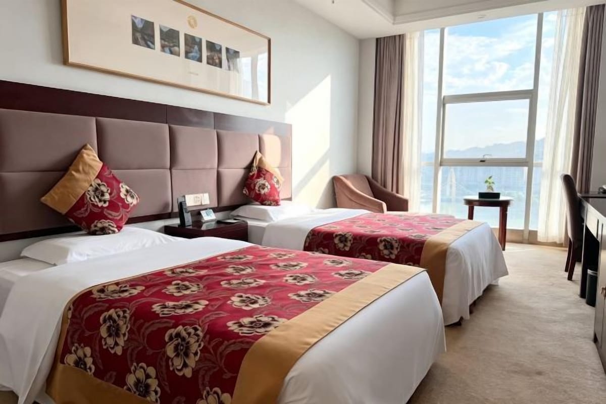 Ein Hotelzimmer mit zwei Betten, einem großen Fenster, einem Schreibtisch und einem Stuhl.