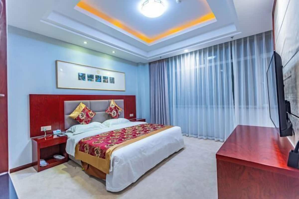 Une chambre d’hôtel avec un grand lit, un bureau, une télévision et un tableau encadré au mur.