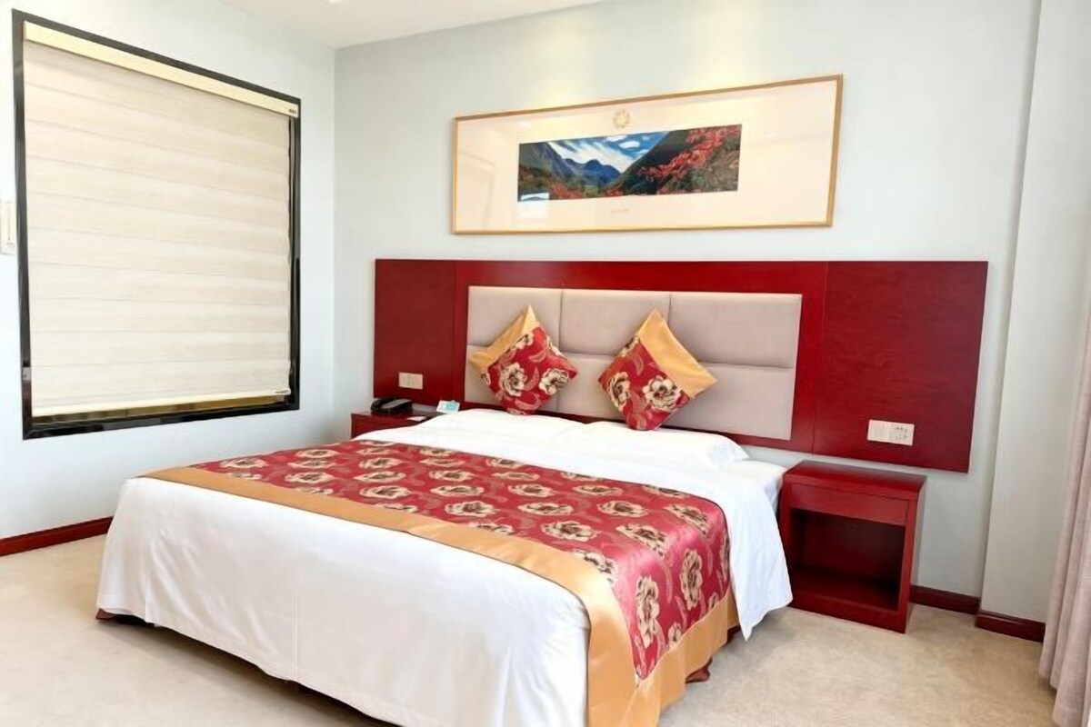 Ein Hotelzimmer mit einem großen Bett, einem Kopfteil mit Dekokissen, einem Nachttisch und einem gerahmten Bild an der Wand.