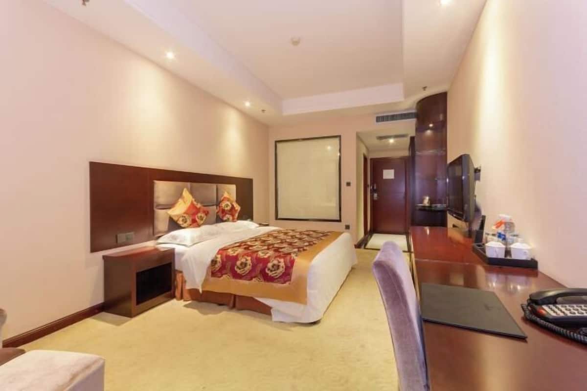 Une chambre d’hôtel comprenant un lit, une table de chevet, un bureau avec une chaise, une télévision et une porte donnant sur une autre pièce.