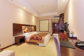 A hotel room with a bed, bedside table, a desk with a chair, a TV, and a door leading to another room.