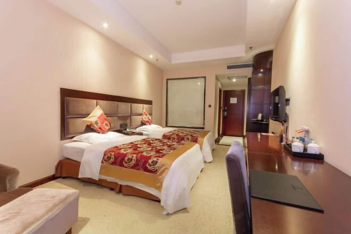 Une chambre d’hôtel avec deux lits, un bureau, une chaise et un téléviseur.