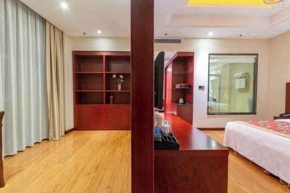 Ein Hotelzimmer mit Holzboden, einem Bett mit weißer Bettdecke, einem Holztisch, einem Fernseher und einem großen Fenster.