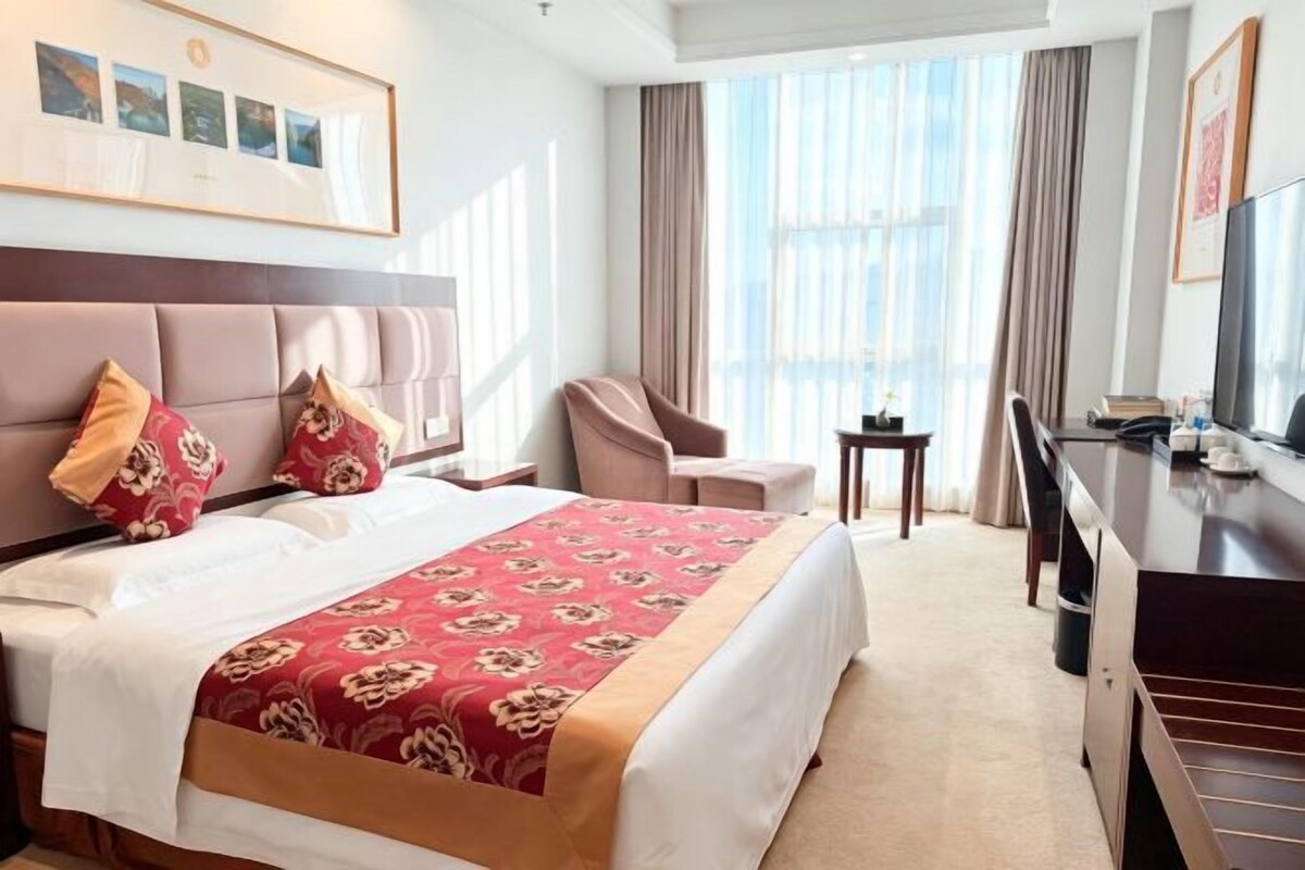 Ein Hotelzimmer mit einem großen Bett, einem Schreibtisch, einem Stuhl und einem Fernseher.