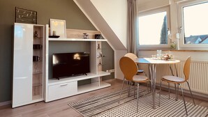 Un salon moderne doté d’un téléviseur à écran plat, d’un coin repas avec deux chaises, d’un escalier et d’une grande fenêtre.
