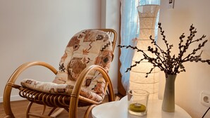 Un fauteuil à bascule en osier avec un coussin à motifs, une petite table sur laquelle est posé un vase rempli de branches et une lampe.