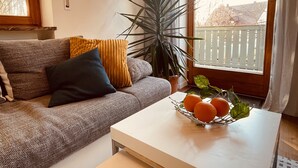 Un salon avec un canapé, une table basse sur laquelle sont posées des oranges et une grande plante.