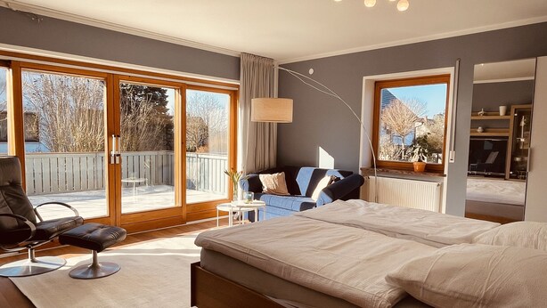 Une chambre avec un grand lit, une chaise, une petite table et une vue sur l’extérieur grâce à une porte coulissante.