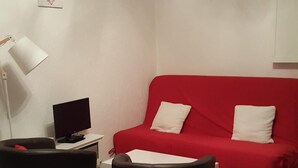 Un soggiorno moderno con un divano rosso, due poltrone nere, una scrivania bianca con un computer e una lampada bianca.